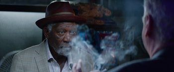 Movie still from “Going in Style” (2017), directed by Zach Braff – An older man wearing a hat and smoking a cigarette; Close Up shot, Over the shoulder angle