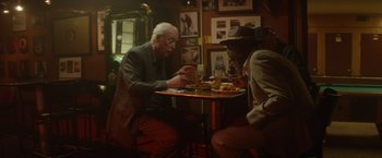 Movie still from “Going in Style” (2017), directed by Zach Braff – A man sitting at a table looking at his cell phone; Medium shot, Low angle