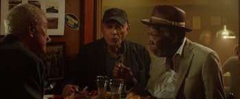 Movie still from “Going in Style” (2017), directed by Zach Braff – Two men sitting at a table with a plate in front of them; Medium shot, Over the shoulder angle