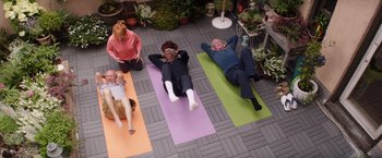 Movie still from “Going in Style” (2017), directed by Zach Braff – A group of people laying on yoga mats on a patio; Wide shot, High angle