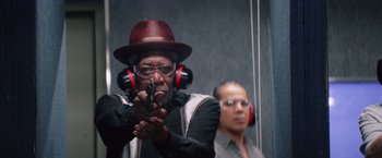 Movie still from “Going in Style” (2017), directed by Zach Braff – A man wearing a hat and holding a gun in his hands; Medium shot, Low angle