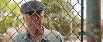 Movie still from “Going in Style” (2017), directed by Zach Braff – An older man looking through a chain link fence; Close Up shot, Over the shoulder angle