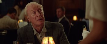 Movie still from “Going in Style” (2017), directed by Zach Braff – An older man sitting at a table in front of a lamp; Close Up shot, Over the shoulder angle