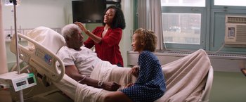 Movie still from “Going in Style” (2017), directed by Zach Braff – An older man and two young women sitting on a hospital bed; Medium shot, Over the shoulder angle