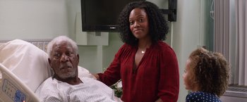Movie still from “Going in Style” (2017), directed by Zach Braff – A woman standing next to an older man in a hospital bed; Medium shot, Over the shoulder angle
