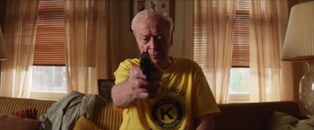 Movie still from “Going in Style” (2017), directed by Zach Braff – An older man holding a gun in a living room; Close Up shot, Low angle