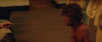 Movie still from “Gold Coast” (2015), directed by Daniel Dencik – A man with curly brown hair is looking at a stick; Close Up shot, High angle