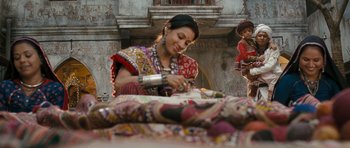 Movie still from “Goliyon Ki Raasleela Ram Leela” (2013), directed by Sanjay Leela Bhansali – A woman in a red and white dress is sewing a quilt; Medium shot, Over the shoulder angle