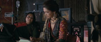 Movie still from “Goliyon Ki Raasleela Ram Leela” (2013), directed by Sanjay Leela Bhansali – A woman in a colorful dress sitting in front of a table; Medium shot, Over the shoulder angle