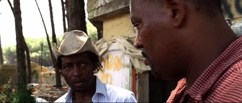 Movie still from “Gomorrah” (2008), directed by Matteo Garrone – Two men standing next to each other in front of a building; Close Up shot, Over the shoulder angle