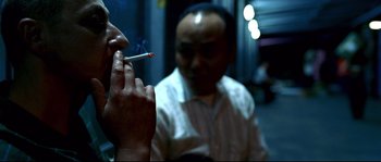 Movie still from “Gomorrah” (2008), directed by Matteo Garrone – A man smoking a cigarette in front of another man; Close Up shot, Over the shoulder angle