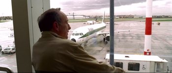 Movie still from “Gomorrah” (2008), directed by Matteo Garrone – A man sitting in front of an airplane on a runway; Medium shot, Low angle