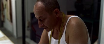 Movie still from “Gomorrah” (2008), directed by Matteo Garrone – A person wearing a tank top with a tape measure around his neck; Close Up shot, Low angle