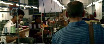 Movie still from “Gomorrah” (2008), directed by Matteo Garrone – A man standing in front of a group of people in a kitchen; Medium shot, Over the shoulder angle