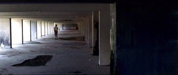 Movie still from “Gomorrah” (2008), directed by Matteo Garrone – A person standing in a building with a lot of pillars; Extreme Wide shot, Low angle