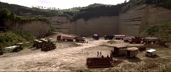 Movie still from “Gomorrah” (2008), directed by Matteo Garrone – A group of people standing near a group of dump trucks; Extreme Wide shot, High angle