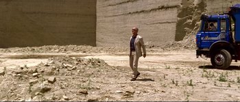 Movie still from “Gomorrah” (2008), directed by Matteo Garrone – A man in a suit and tie walking in a field; Wide shot, Low angle