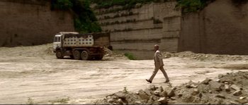 Movie still from “Gomorrah” (2008), directed by Matteo Garrone – A man in a suit walks in front of a dump truck; Extreme Wide shot, High angle