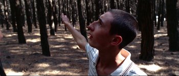 Movie still from “Gomorrah” (2008), directed by Matteo Garrone – A young man in the woods with his arm outstreched; Medium shot, Low angle