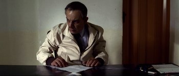 Movie still from “Gomorrah” (2008), directed by Matteo Garrone – A man sitting at a table looking at a piece of paper; Medium shot, Low angle