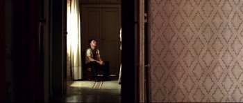 Movie still from “Gomorrah” (2008), directed by Matteo Garrone – A man sitting on a chair in a room; Wide shot, High angle