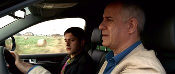 Movie still from “Gomorrah” (2008), directed by Matteo Garrone – A man and a man in a car looking out the window; Close Up shot, Over the shoulder angle