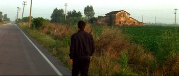 Movie still from “Gomorrah” (2008), directed by Matteo Garrone – A man standing on the side of a road near a field; Wide shot, Low angle