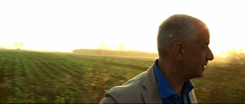 Movie still from “Gomorrah” (2008), directed by Matteo Garrone – A man in a jacket and a blue shirt riding a train; Close Up shot, Low angle