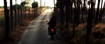 Movie still from “Gomorrah” (2008), directed by Matteo Garrone – Two people riding a motorcycle down a street; Wide shot, Low angle