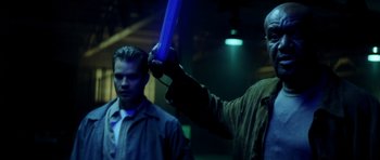 Movie still from “Gone in 60 Seconds” (2000), directed by Dominic Sena – A man holding a blue object in a dark room; Medium shot, Over the shoulder angle