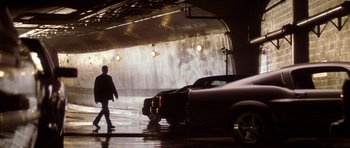 Movie still from “Gone in 60 Seconds” (2000), directed by Dominic Sena – A man walking in front of two cars in a garage; Wide shot, Low angle