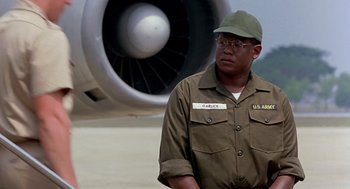 Movie still from “Good Morning, Vietnam” (1987), directed by Barry Levinson – A man in a uniform standing in front of an airplane; Medium shot, Over the shoulder angle