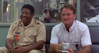 Movie still from “Good Morning, Vietnam” (1987), directed by Barry Levinson – A couple of men sitting next to each other holding cups; Medium shot, Over the shoulder angle