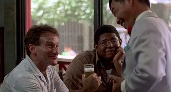 Movie still from “Good Morning, Vietnam” (1987), directed by Barry Levinson – A group of men sitting at a table with a beer; Medium shot, Over the shoulder angle