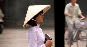 Movie still from “Good Morning, Vietnam” (1987), directed by Barry Levinson – A woman wearing a straw hat while holding a book; Medium shot, Over the shoulder angle