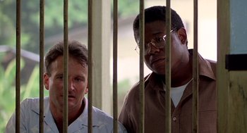 Movie still from “Good Morning, Vietnam” (1987), directed by Barry Levinson – Two men standing next to each other behind bars; Medium shot, Low angle