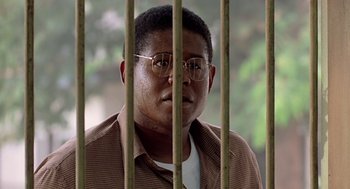 Movie still from “Good Morning, Vietnam” (1987), directed by Barry Levinson – A man with glasses behind bars looking at the camera; Close Up shot, Low angle