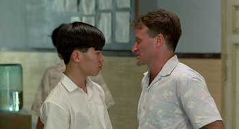 Movie still from “Good Morning, Vietnam” (1987), directed by Barry Levinson – A man standing next to another man in a room; Close Up shot, Over the shoulder angle