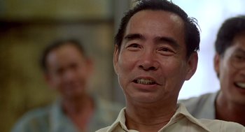 Movie still from “Good Morning, Vietnam” (1987), directed by Barry Levinson – An older asian man smiling at the camera; Close Up shot, Low angle