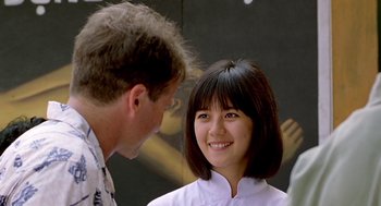 Movie still from “Good Morning, Vietnam” (1987), directed by Barry Levinson – A man standing next to a woman in front of a painting; Close Up shot, Over the shoulder angle