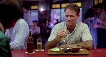 Movie still from “Good Morning, Vietnam” (1987), directed by Barry Levinson – A man sitting at a table with a plate of food; Medium shot, Over the shoulder angle
