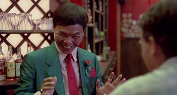 Movie still from “Good Morning, Vietnam” (1987), directed by Barry Levinson – A man wearing a green suit and a red tie laughing; Close Up shot, Over the shoulder angle