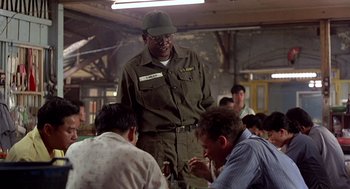 Movie still from “Good Morning, Vietnam” (1987), directed by Barry Levinson – A man standing in front of a group of people; Medium shot, Over the shoulder angle