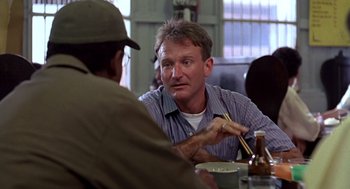 Movie still from “Good Morning, Vietnam” (1987), directed by Barry Levinson – A man sitting at a table with a bowl of food; Close Up shot, Over the shoulder angle