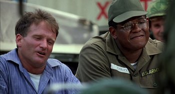 Movie still from “Good Morning, Vietnam” (1987), directed by Barry Levinson – Two men sitting next to each other on a table; Close Up shot, Low angle