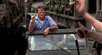 Movie still from “Good Morning, Vietnam” (1987), directed by Barry Levinson – A man sitting in the back of an army vehicle; Medium shot, Over the shoulder angle