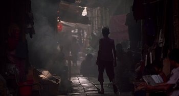 Movie still from “Good Morning, Vietnam” (1987), directed by Barry Levinson – A person walking down a street with smoke coming out of a building; Wide shot, High angle