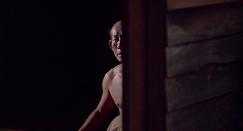 Movie still from “Good Morning, Vietnam” (1987), directed by Barry Levinson – A man standing next to a wall in a dark room; Medium shot, Low angle