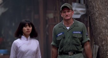 Movie still from “Good Morning, Vietnam” (1987), directed by Barry Levinson – A man and a woman standing next to each other in front of a building; Medium shot, Low angle