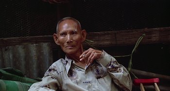 Movie still from “Good Morning, Vietnam” (1987), directed by Barry Levinson – An older man sitting in front of a wooden fence; Close Up shot, Low angle